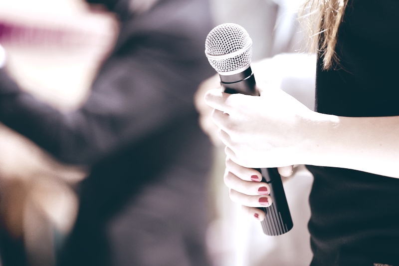 Woman stands on stage with microphone Woman stands on stage with microphone