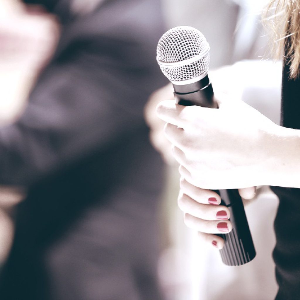 Woman stands on stage with microphone Woman stands on stage with microphone